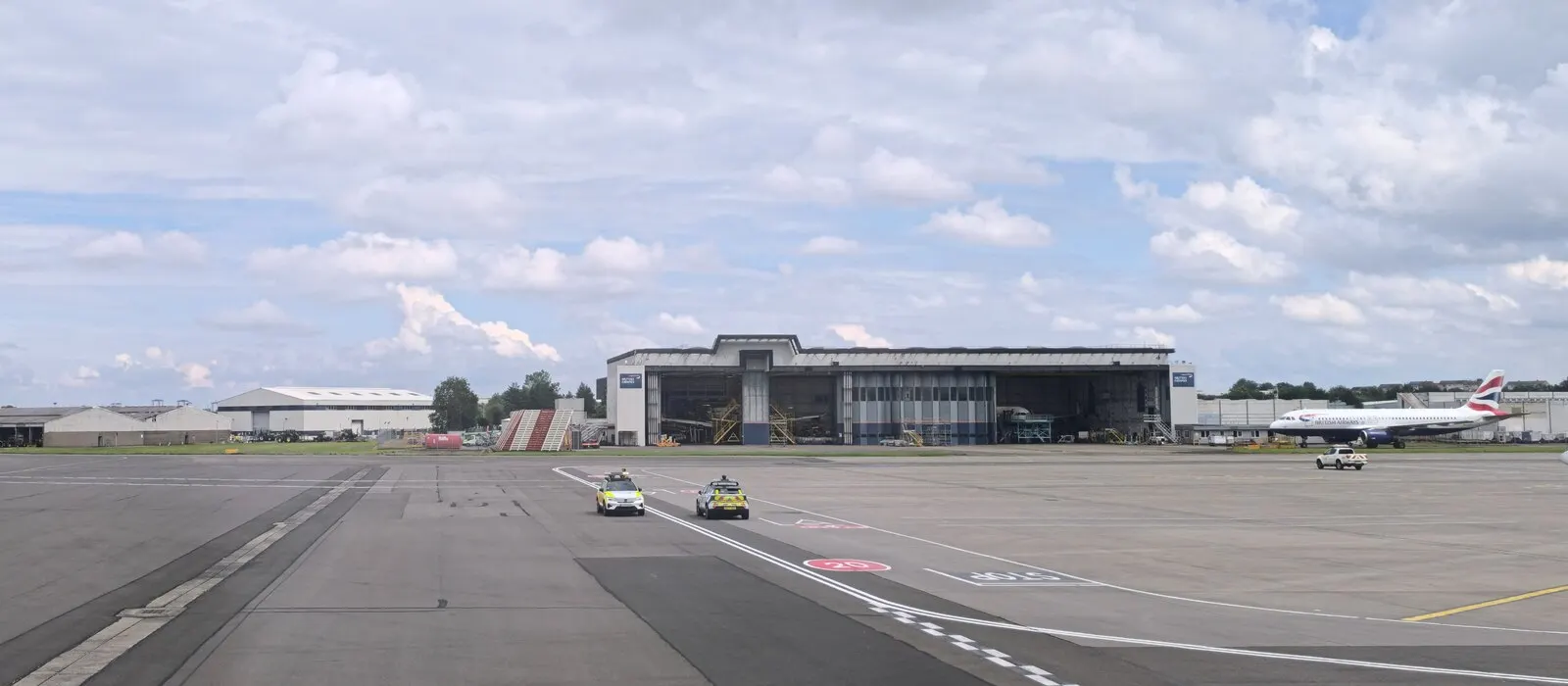 A large British Airways maintenance hangar on the airfield at Glasgow Airport, with open bays facing the tarmac.