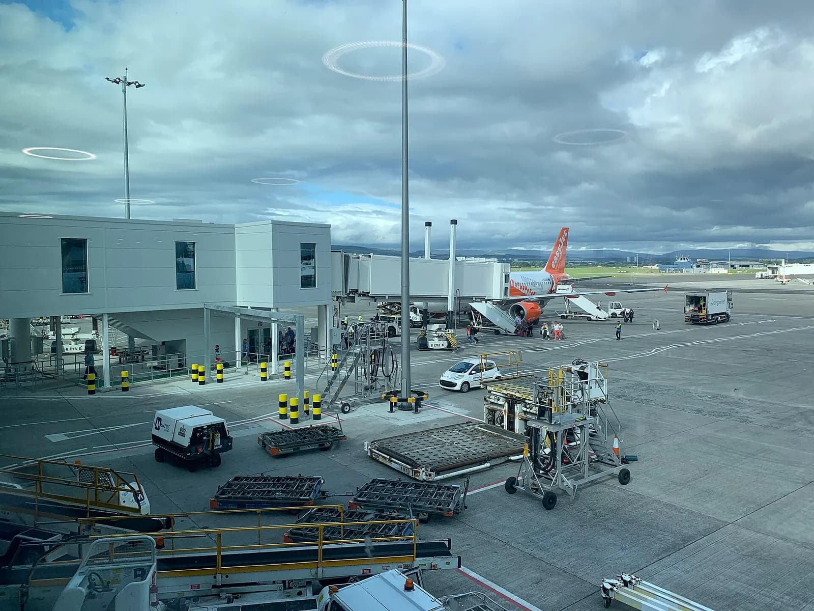 View through large terminal windows from a waiting area onto the apron, with parked aircraft and ground equipment visible outside.