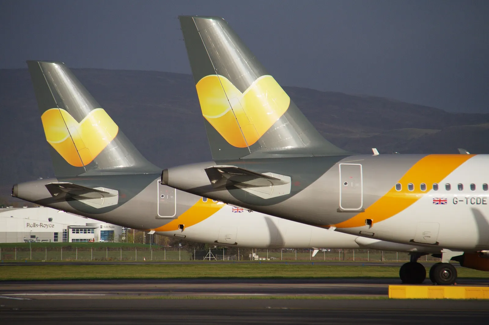 A line of aircraft tail fins from different airlines parked together on the ramp at Glasgow Airport.