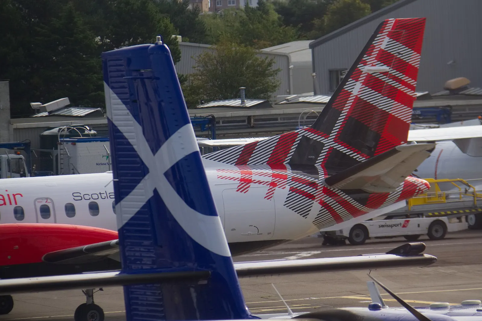 Close view of two aircraft tails with Scottish branding, including Loganair and Highland Airways liveries, at Glasgow Airport.