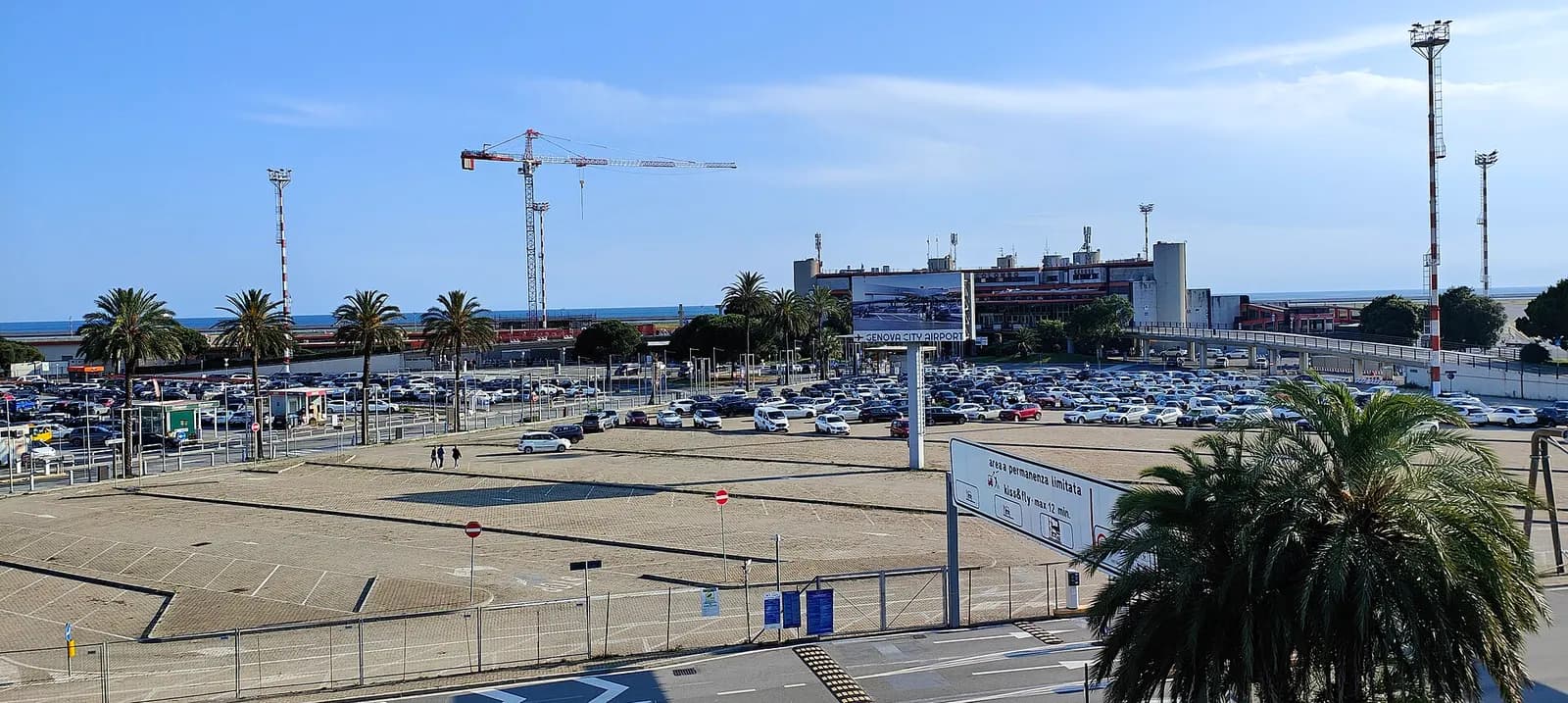 Genova City Airport terminal and parking from the approach road, with sea behind the building and construction crane