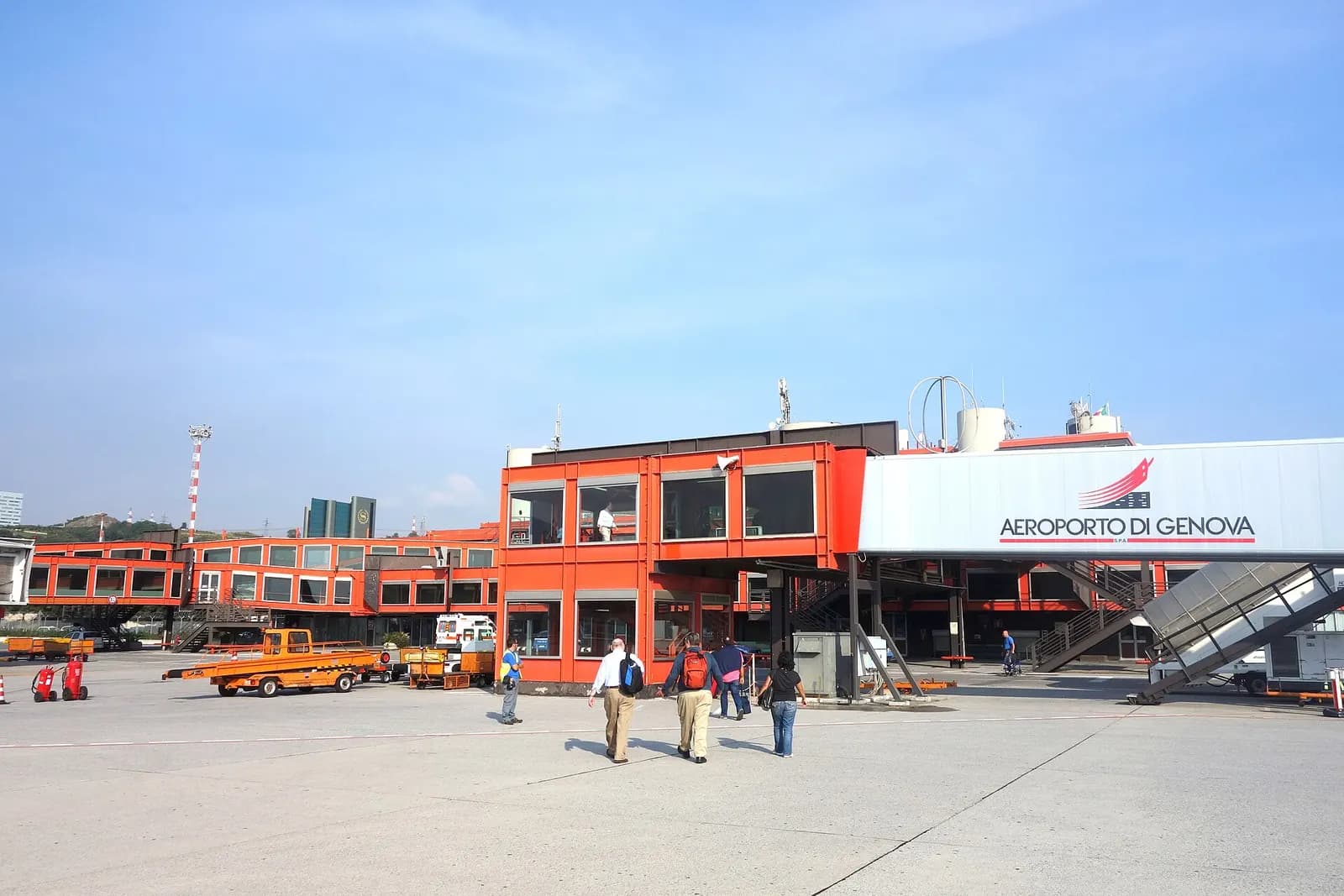 Airside apron and red-orange terminal modules at Genoa Cristoforo Colombo Airport with jet bridge branding