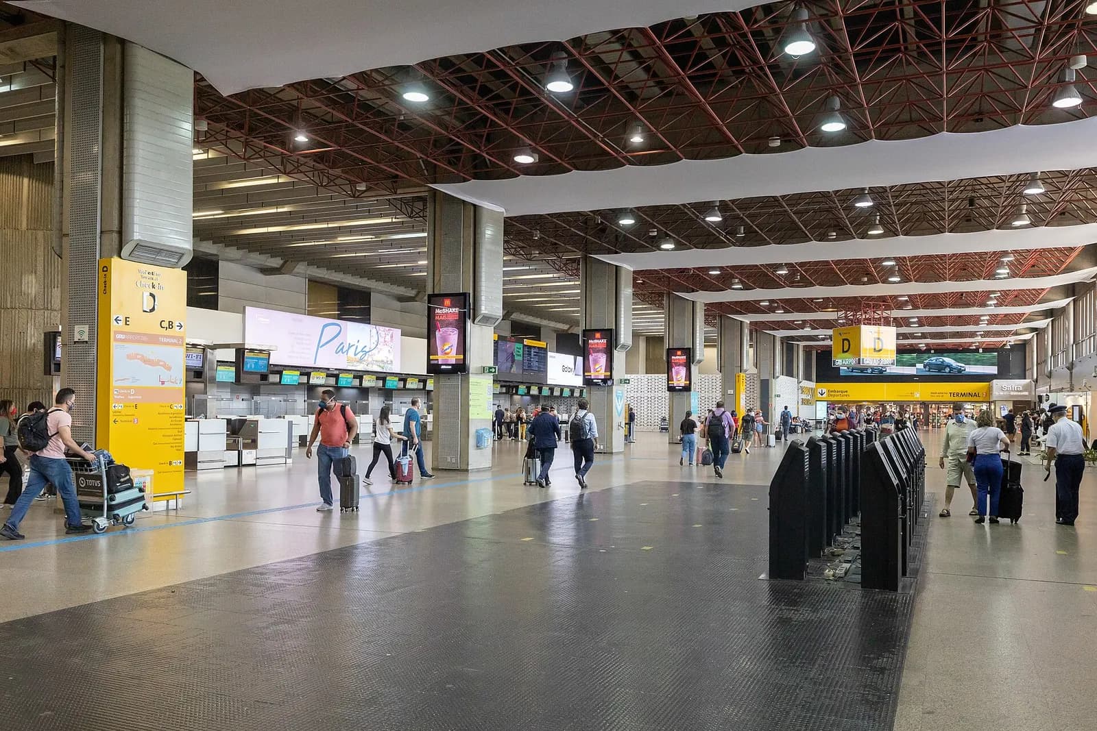 Passengers at check-in counters beneath departure boards in Terminal 2 check-in area D at GRU.