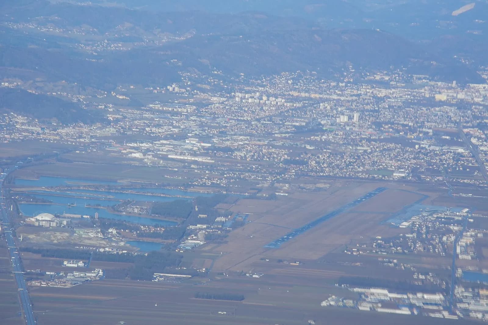 High oblique aerial of Graz Airport with Feldkirchen, lakes, and hills beyond