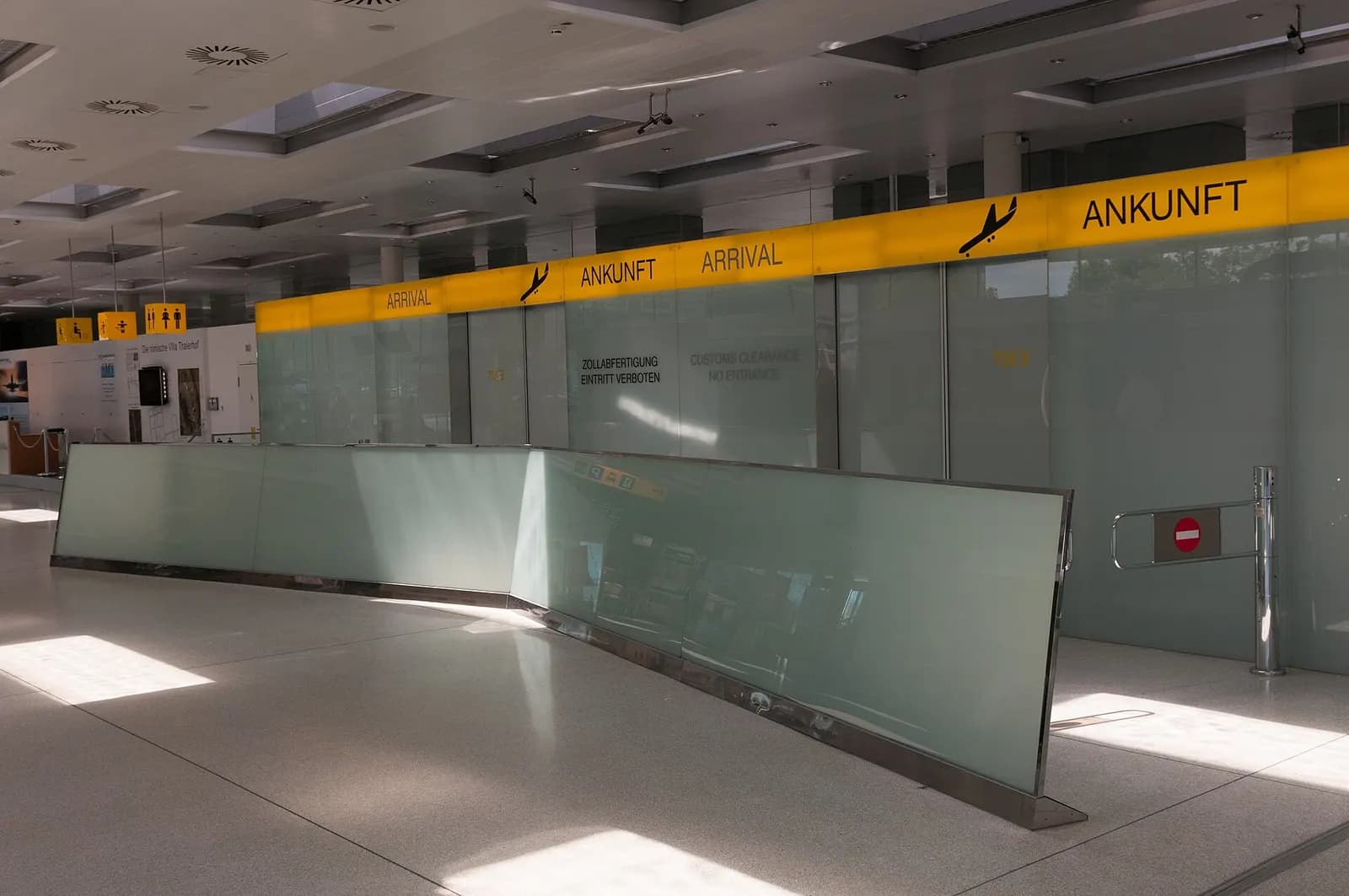 Arrivals glass partition marked ANKUNFT ARRIVAL and customs no-entry doors