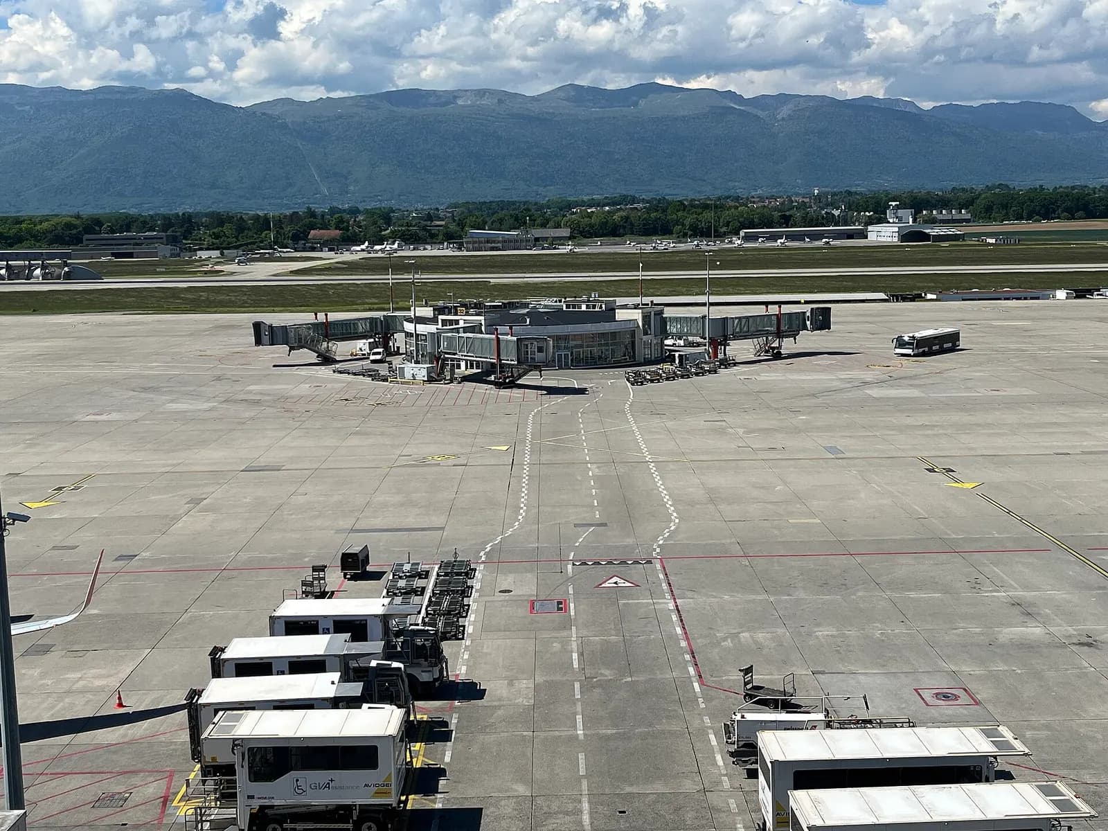 A long glass-walled satellite boarding pier at Geneva Airport with jet bridges and aircraft parked outside.