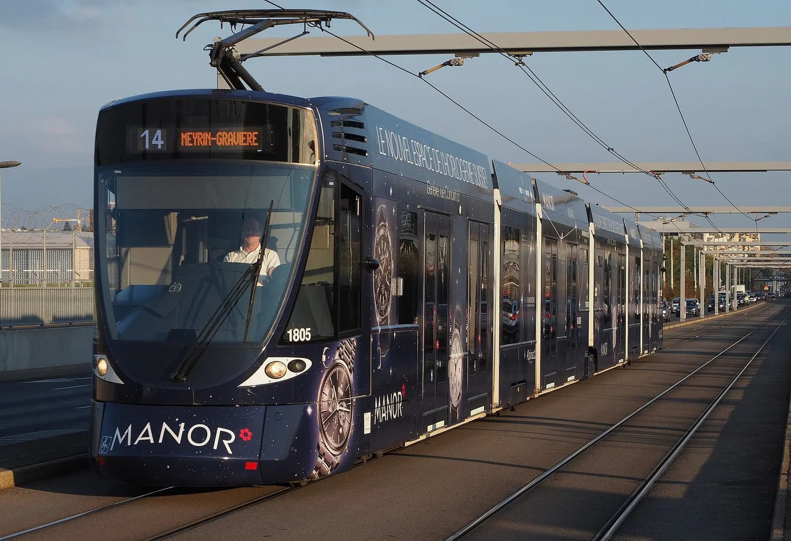 A Stadler Tango tram on lowered overhead wires traveling on a street in the immediate vicinity of Geneva Airport.