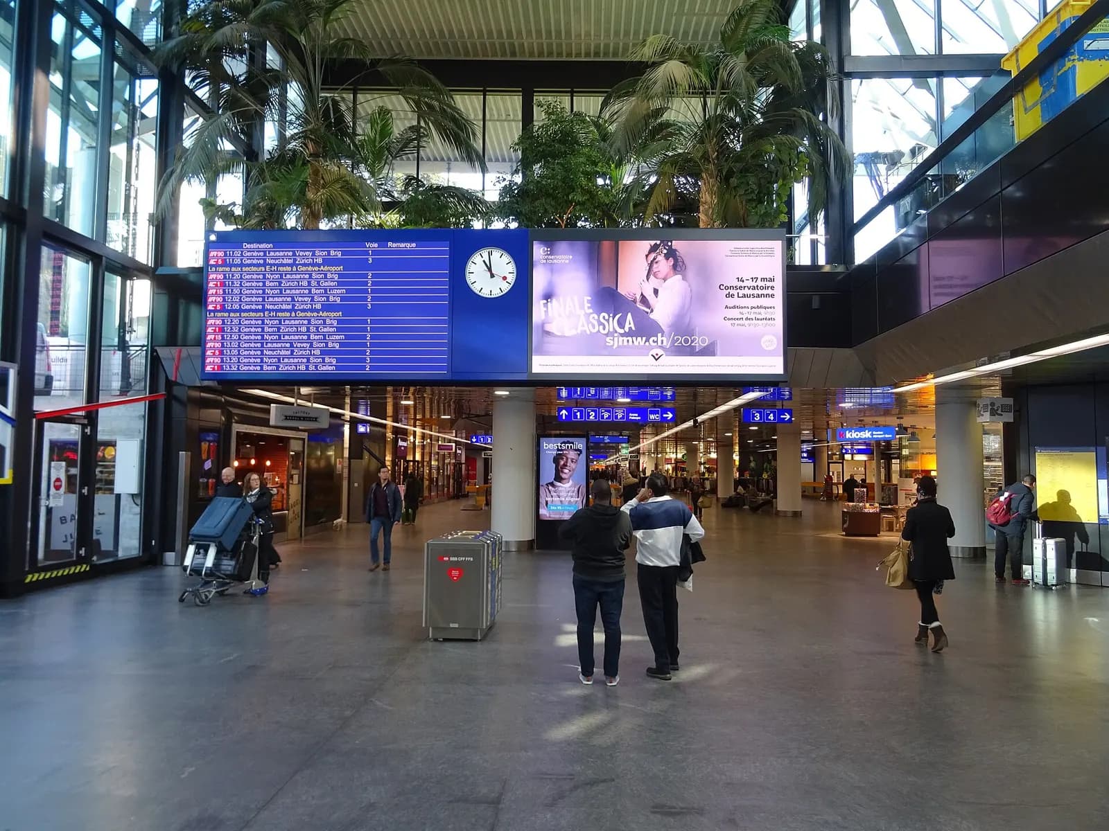 A digital departures board listing train times in the main hall of Genève-Aéroport railway station.