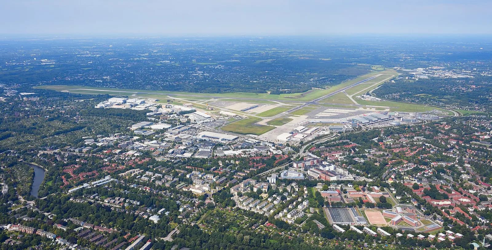 A high-altitude aerial photograph of Hamburg Airport showing parallel runways, taxiways, and terminal clusters.