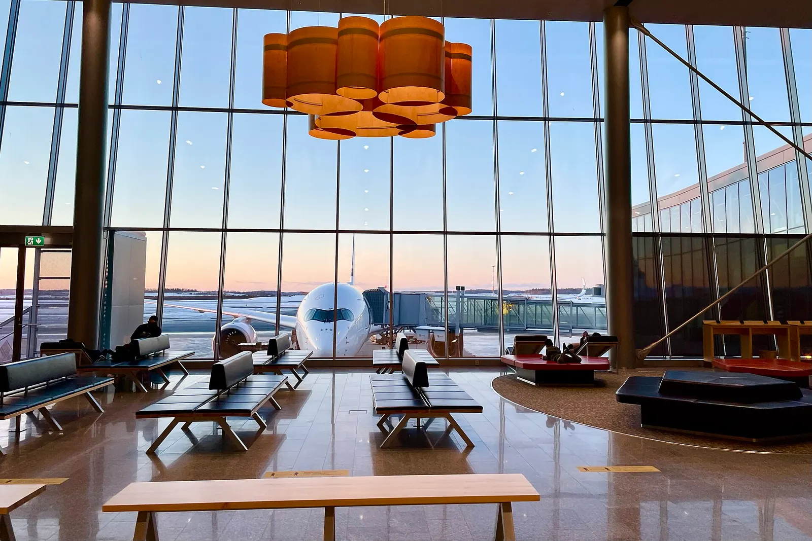 A wide terminal walkway with floor-to-ceiling windows looking out at a Finnair Airbus A350 parked at the gate.