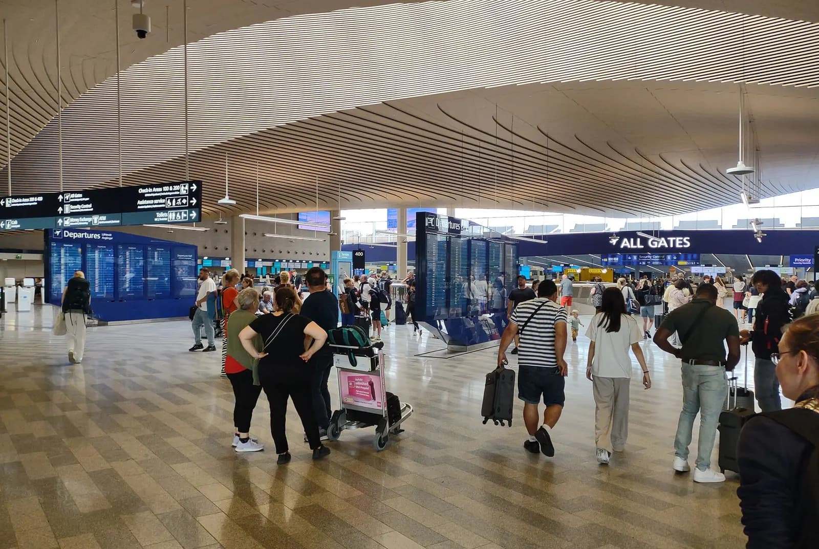 The main check-in hall with rows of self-service kiosks, baggage-drop belts, and overhead flight information displays.