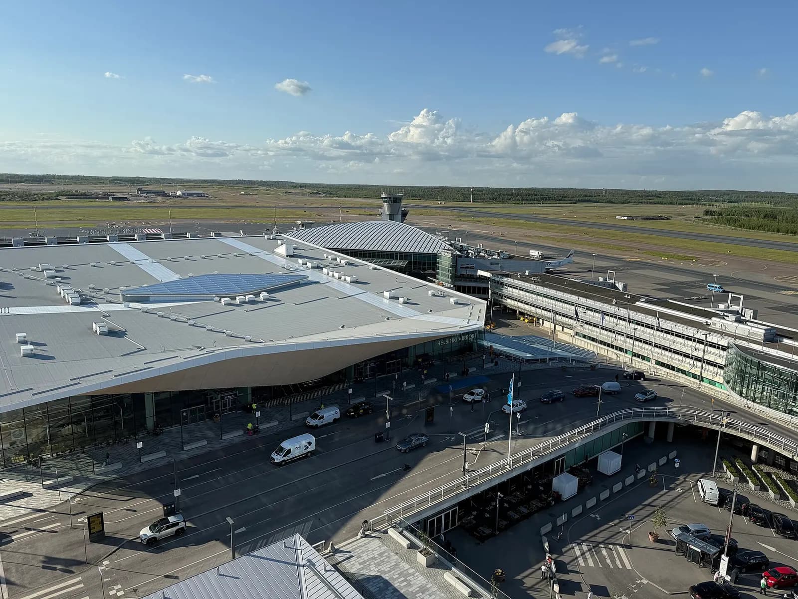 Aerial view of Helsinki-Vantaa showing the expanded terminal complex, apron, and runways amid surrounding forest.