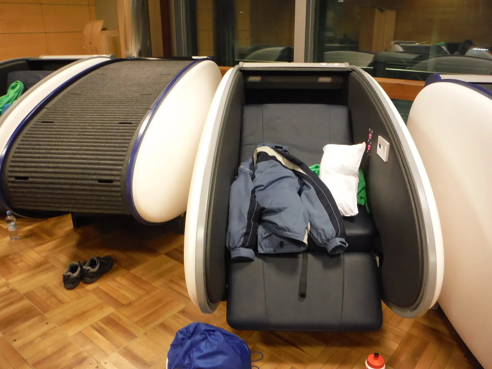 A row of enclosed sleeping pods with curved walls installed along a quiet corridor near the gates.