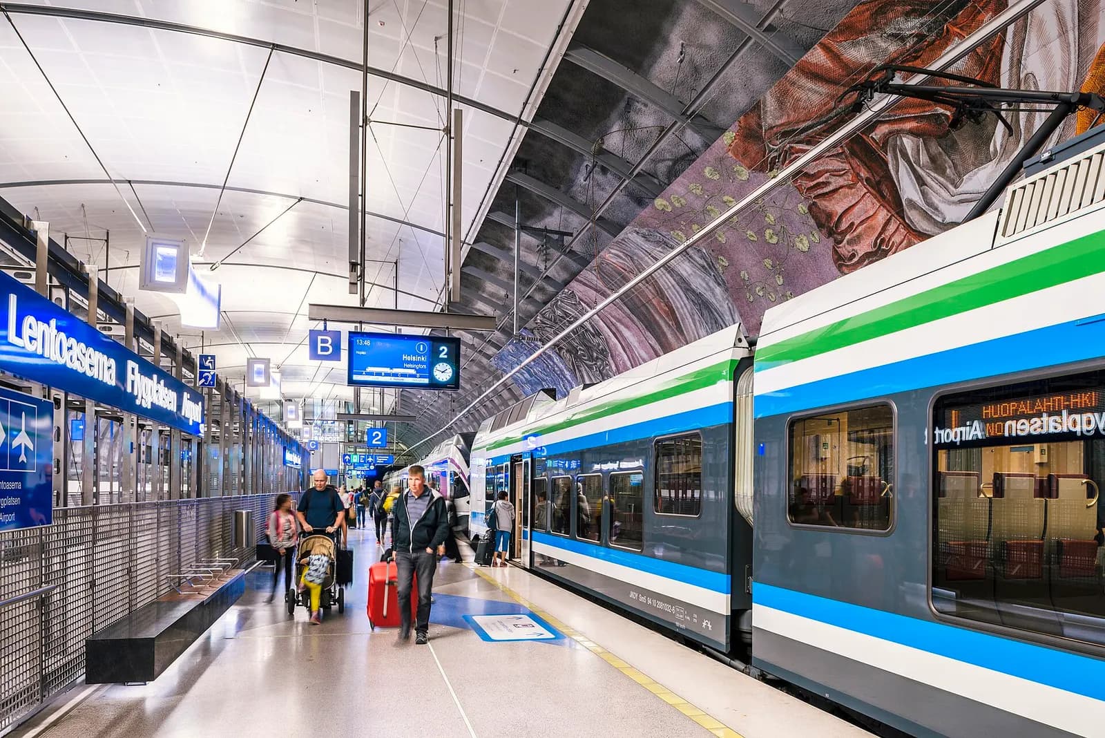 The underground Helsinki Airport railway station platform with a train stopped at the sheltered boarding area.