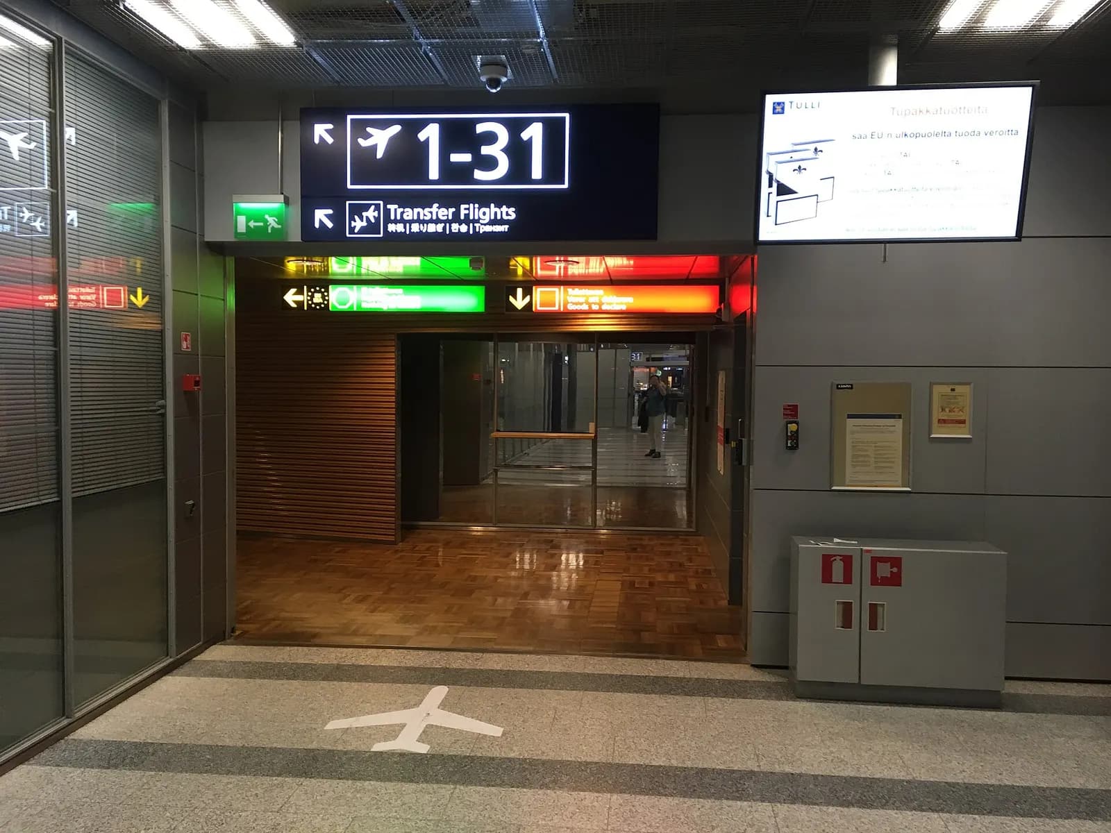 Overhead airport signage marking the transfer-flights corridor with directional arrows in the connecting walkway.