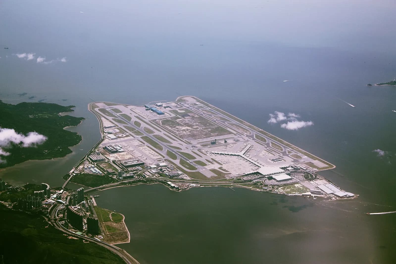Aerial view of Hong Kong International Airport on Chek Lap Kok island, with runways, terminals, and surrounding sea visible from above.