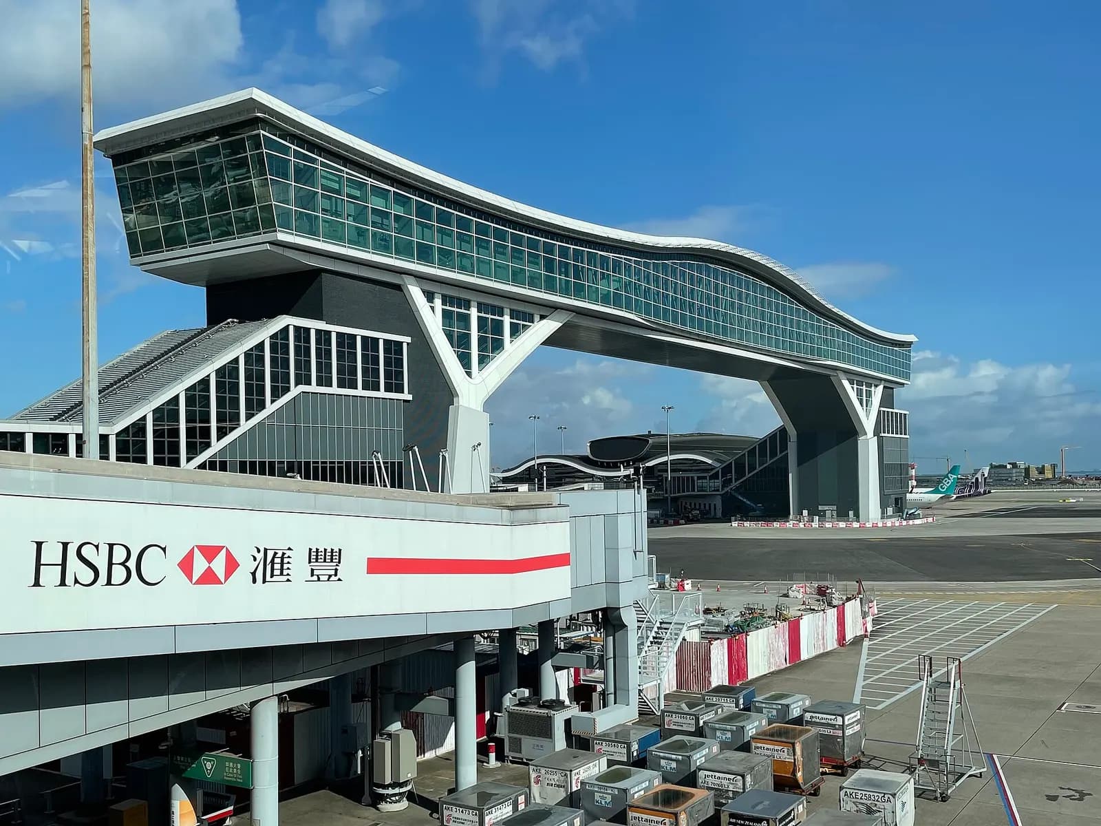 The glass-enclosed SkyBridge spans above the apron, connecting Terminal 1 to the North Satellite Concourse.