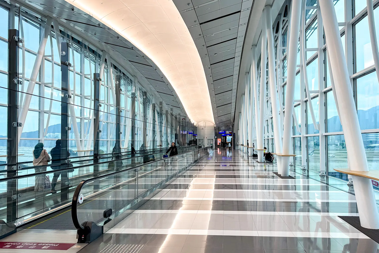 Inside the SkyBridge walkway with panoramic windows overlooking parked aircraft and the airfield below.