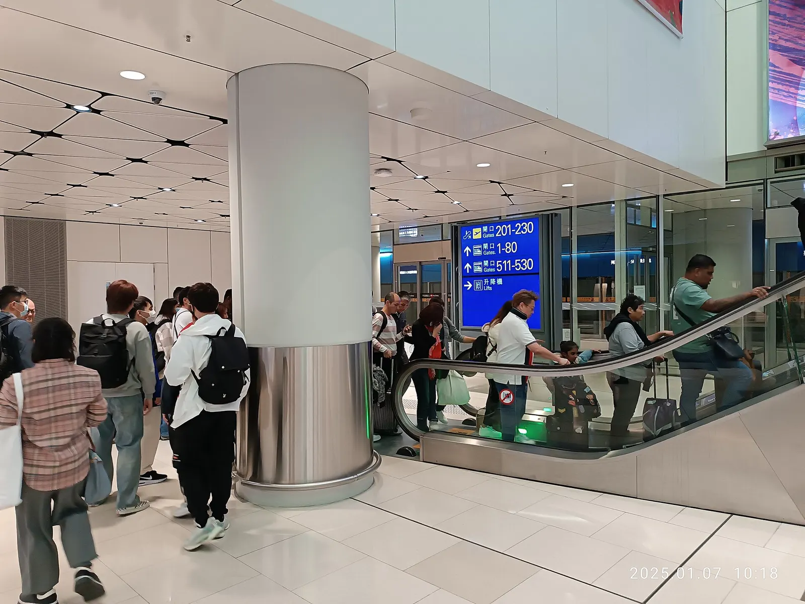 Travelers on escalators in the Terminal 1 departure concourse beneath curved skylights and directional signs.