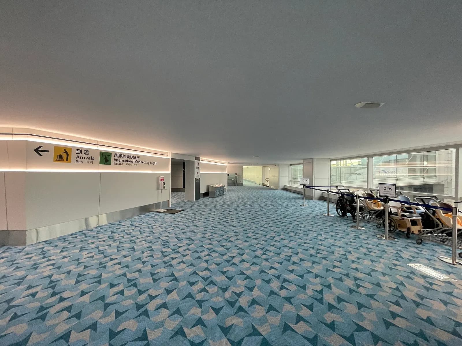 Spacious international arrivals mezzanine at Terminal 2 with high ceilings, glass walls, and passengers walking toward baggage claim.