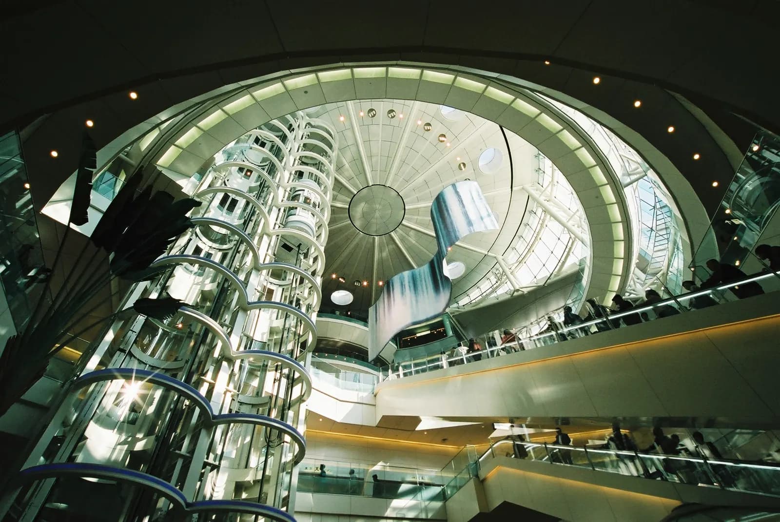 Multi-story open atrium in Terminal 2 leading to the marketplace area, with escalators, shops, and natural light from above.