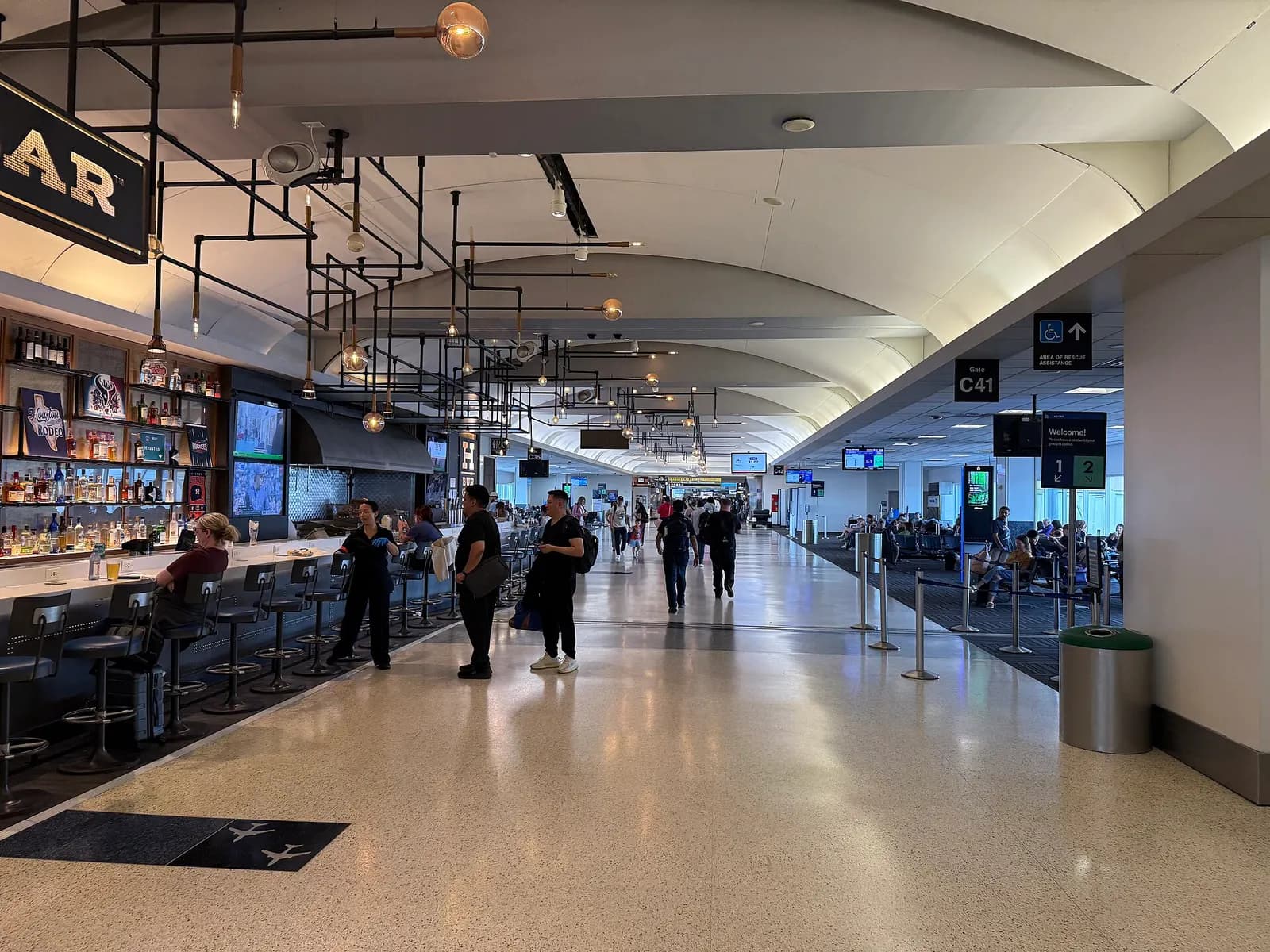 Wide view of the bright, modern interior concourse in Terminal C with high ceilings, glass walls, moving walkways, and travelers walking with luggage.