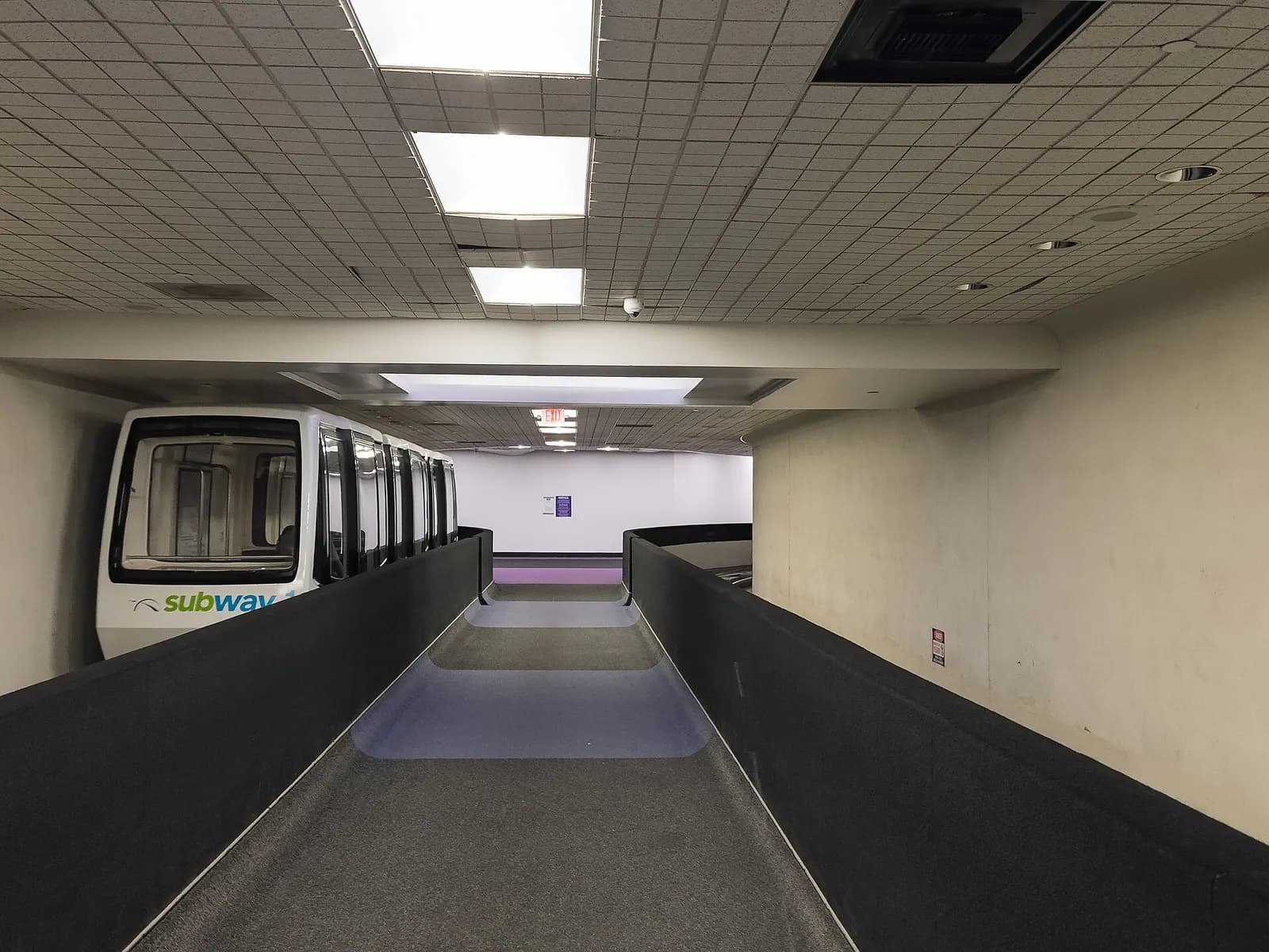 An underground subway train at a station beneath George Bush Intercontinental Airport with platform signage and fluorescent lighting.