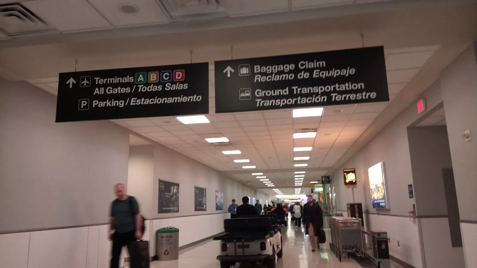 Spacious interior of Terminal E with check-in counters, tall windows, and passengers moving through the departures hall.