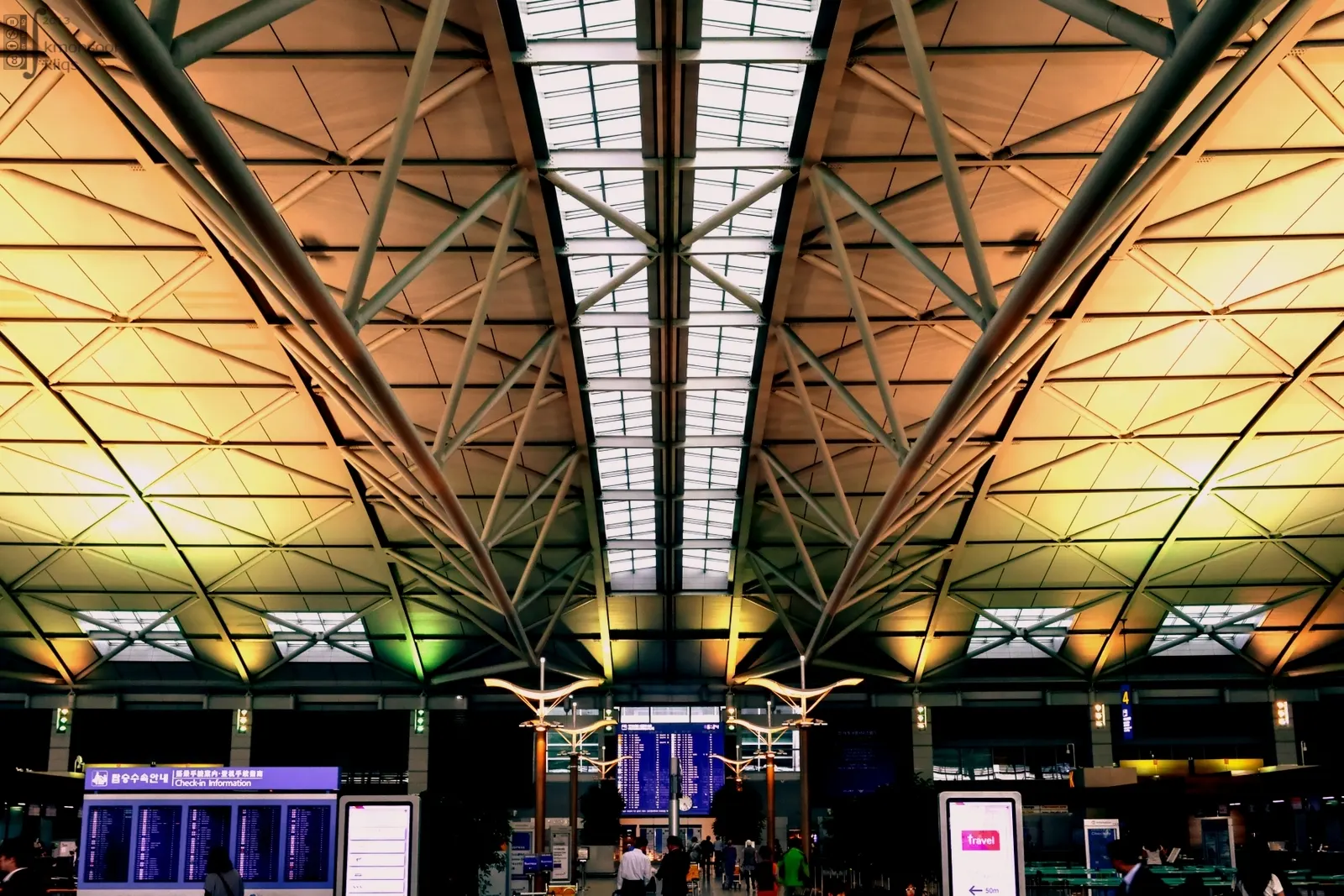 Spacious Terminal 1 concourse at Incheon International Airport with high curved ceilings, bright natural light, and travelers walking beneath large departure boards.