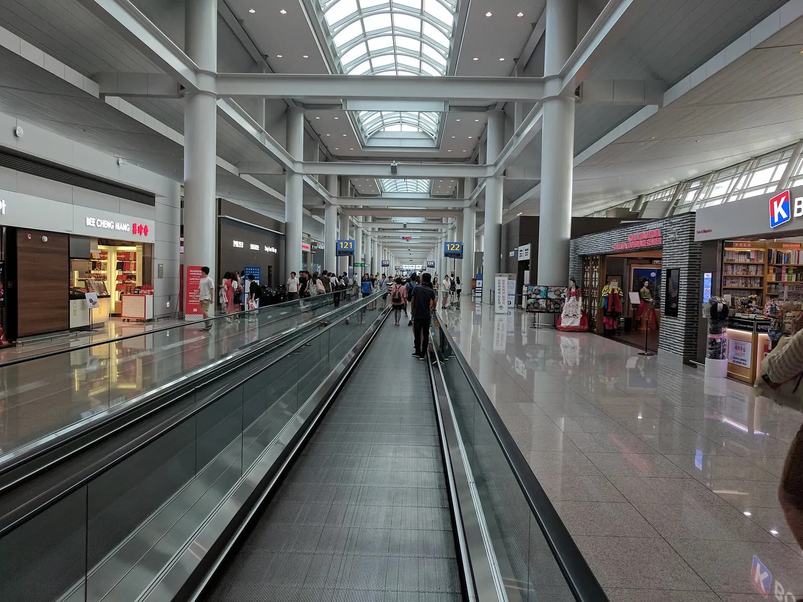 Travelers ride a moving walkway through a long, bright corridor inside Incheon International Airport.