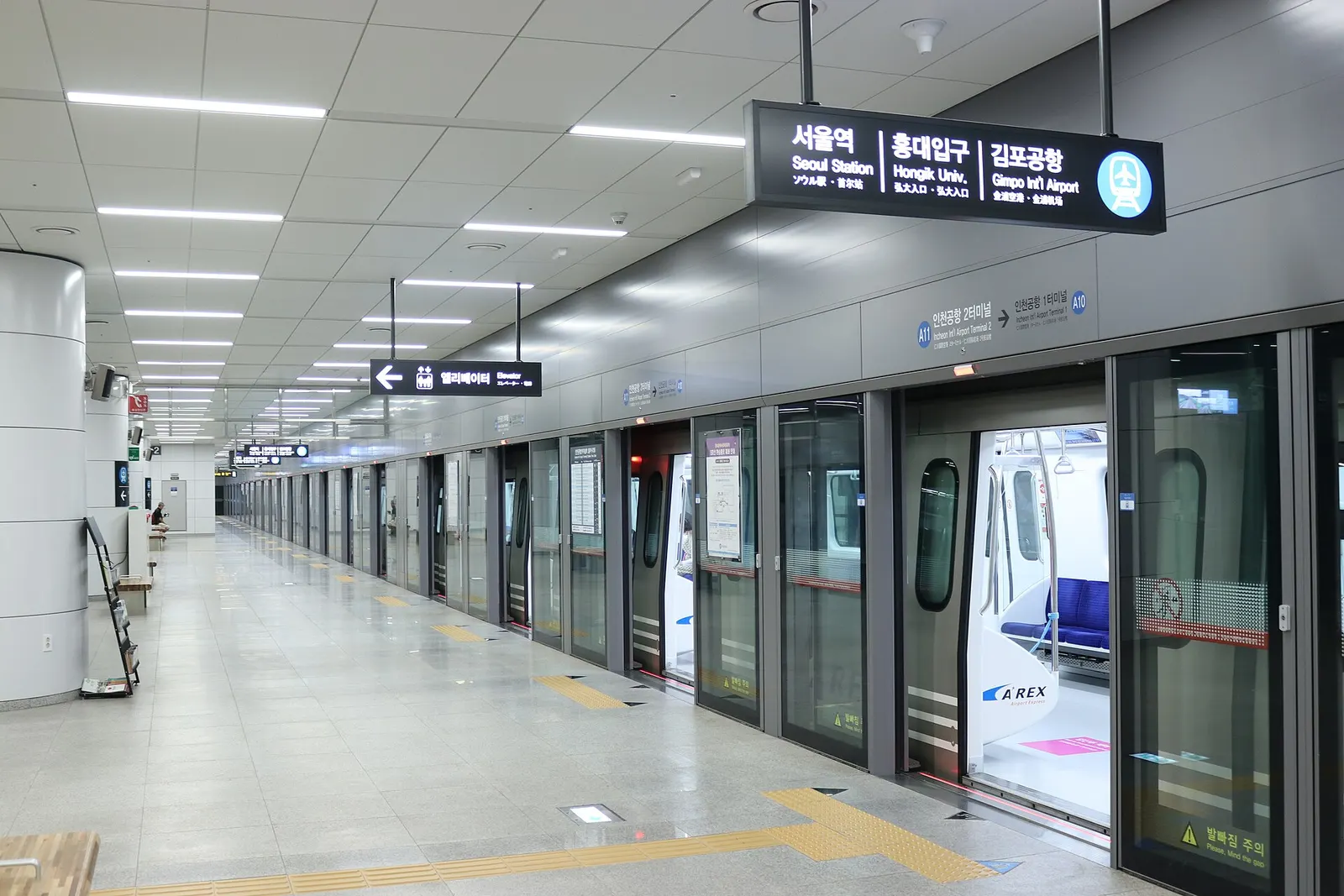 The train platform at Incheon Airport Terminal 2 Station with tracks, a waiting area, and signs for airport rail services.