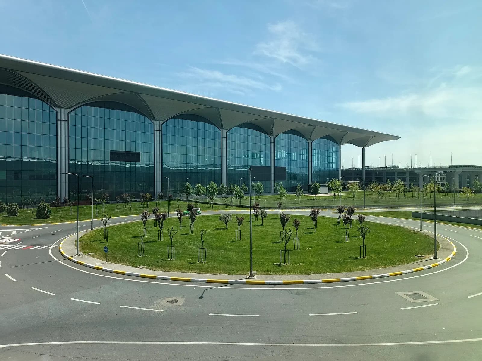 Modern Istanbul Airport terminal building and a circular road interchange seen from the approach on a clear day.