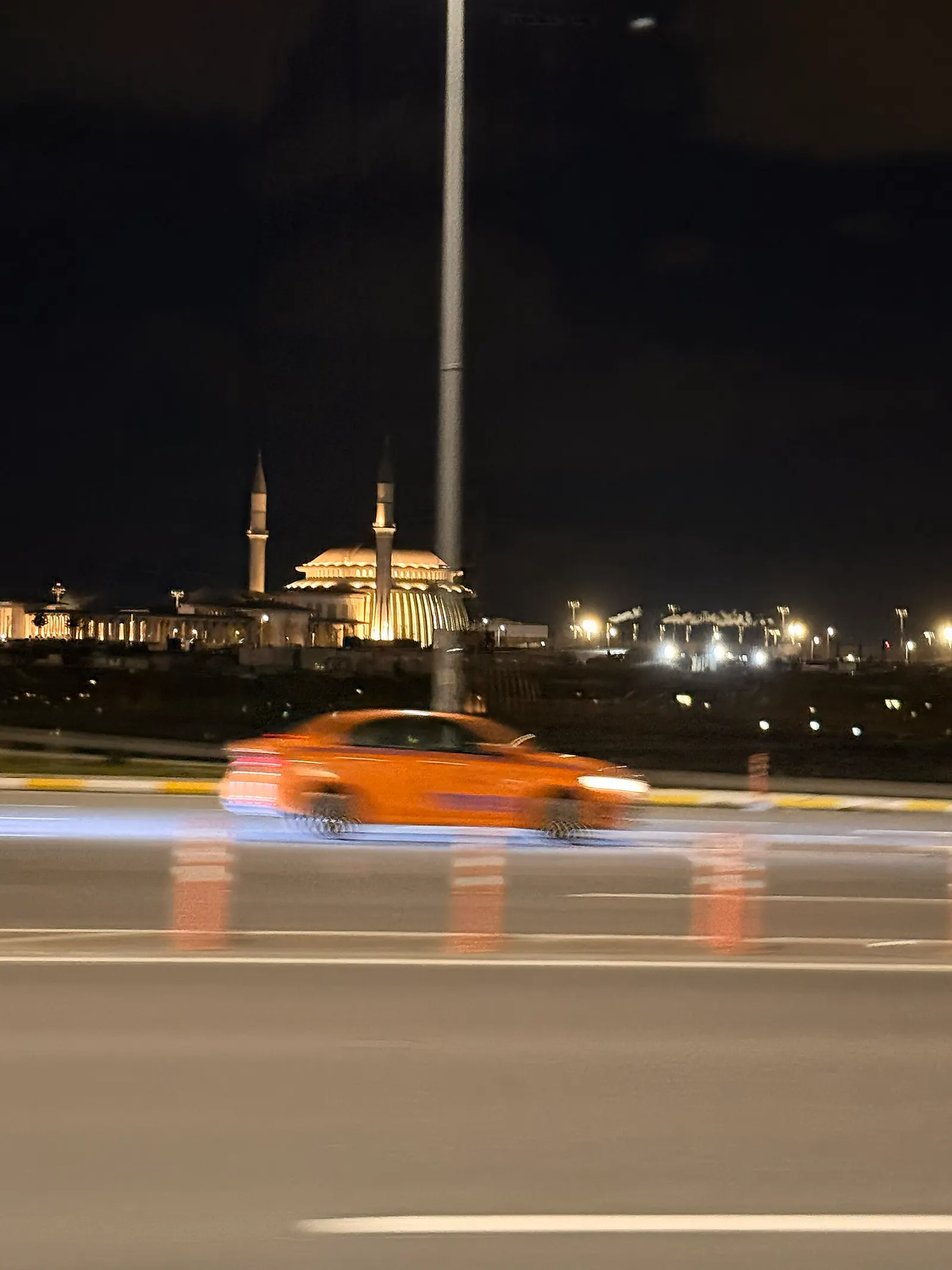Istanbul Airport Mosque illuminated at night with its dome, minaret, and courtyard visible against the dark sky.