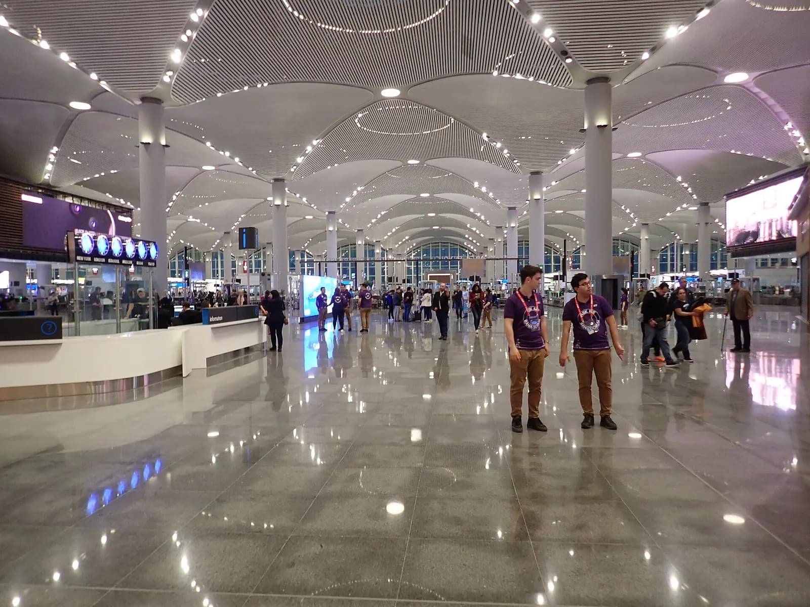 Spacious glass-walled departure hall inside Istanbul Airport with high ceilings, shops, and travelers walking the concourse.