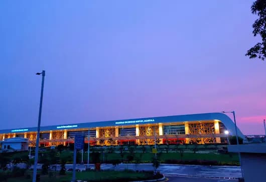 Twilight exterior of Maharaja Bir Bikram Airport, Agartala, with illuminated facade lettering and tree-motif columns.