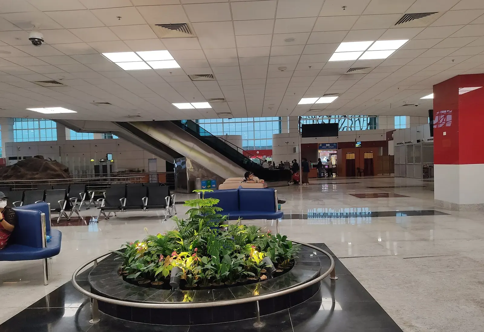 Interior of Agartala’s integrated terminal hall with seating, circular planter, escalator, and bilingual Exit / Arrivals signage.