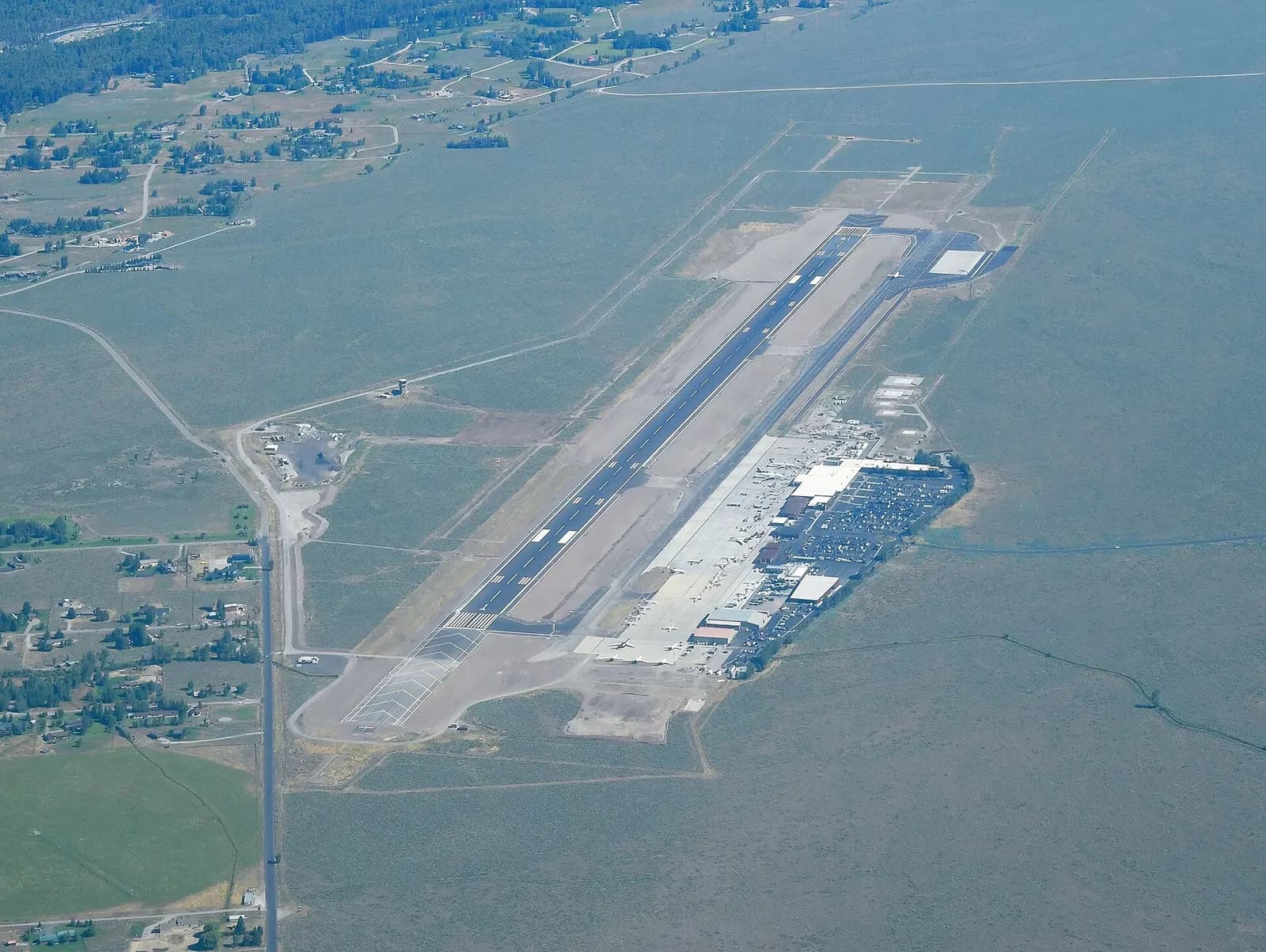 August 2022 aerial of Jackson Hole Airport looking across the single runway and civil terminal campus inside Grand Teton National Park.