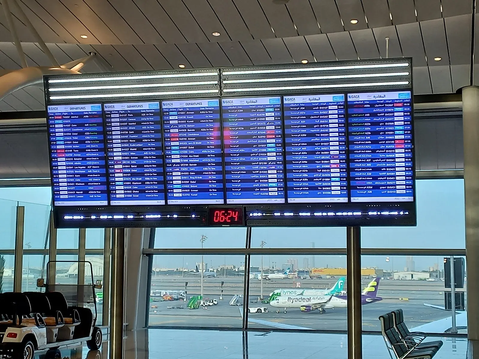 Large digital departure boards listing flight numbers, destinations, and gate assignments hang above seating in the terminal.