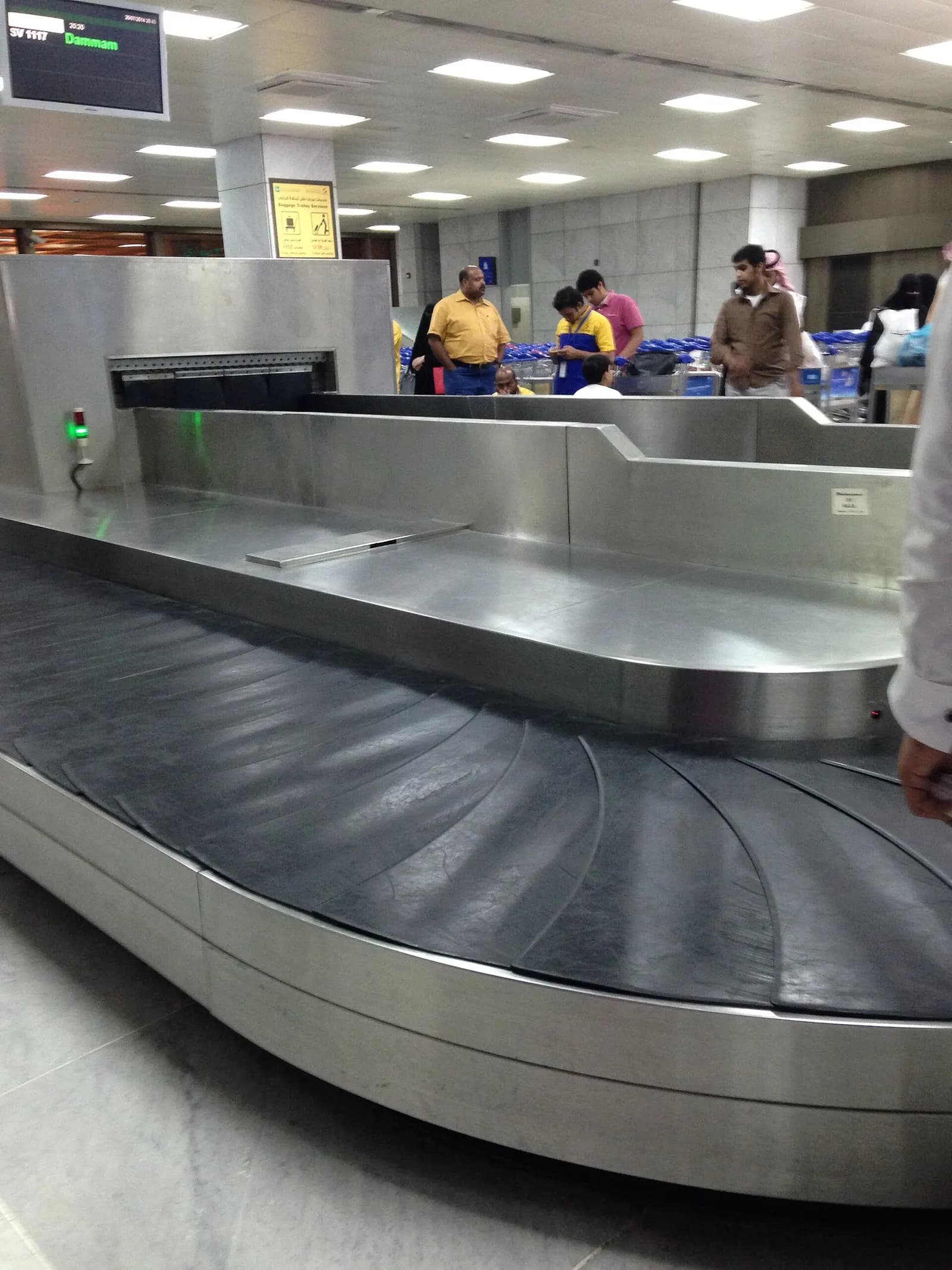 Passengers stand around a baggage carousel in the arrivals hall as suitcases move along the rotating belt.