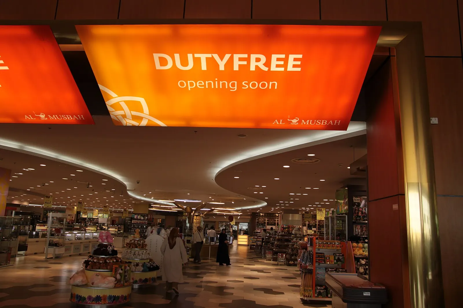 Duty-free shops with illuminated brand signs line a wide pedestrian corridor inside the Jeddah airport terminal.