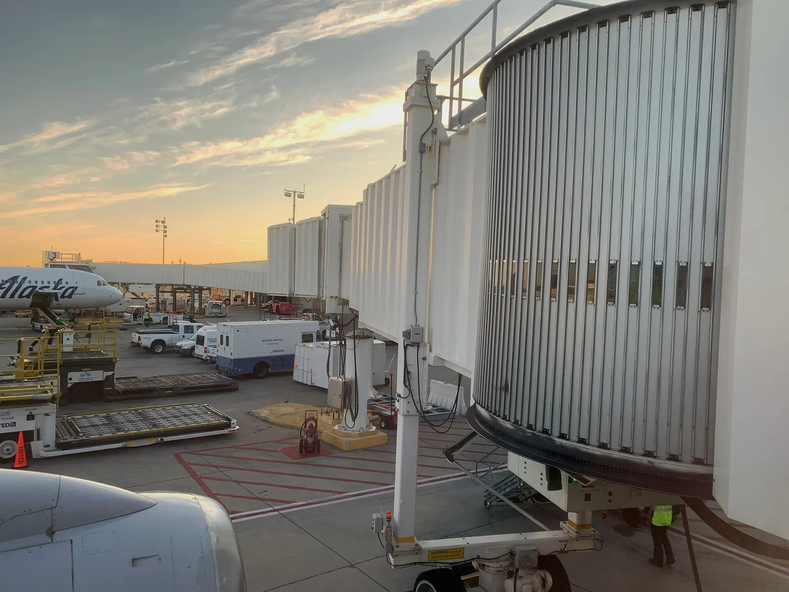 A row of passenger jet bridges extends from Terminal 7's gate area in the early morning light, with parked aircraft at the stands.