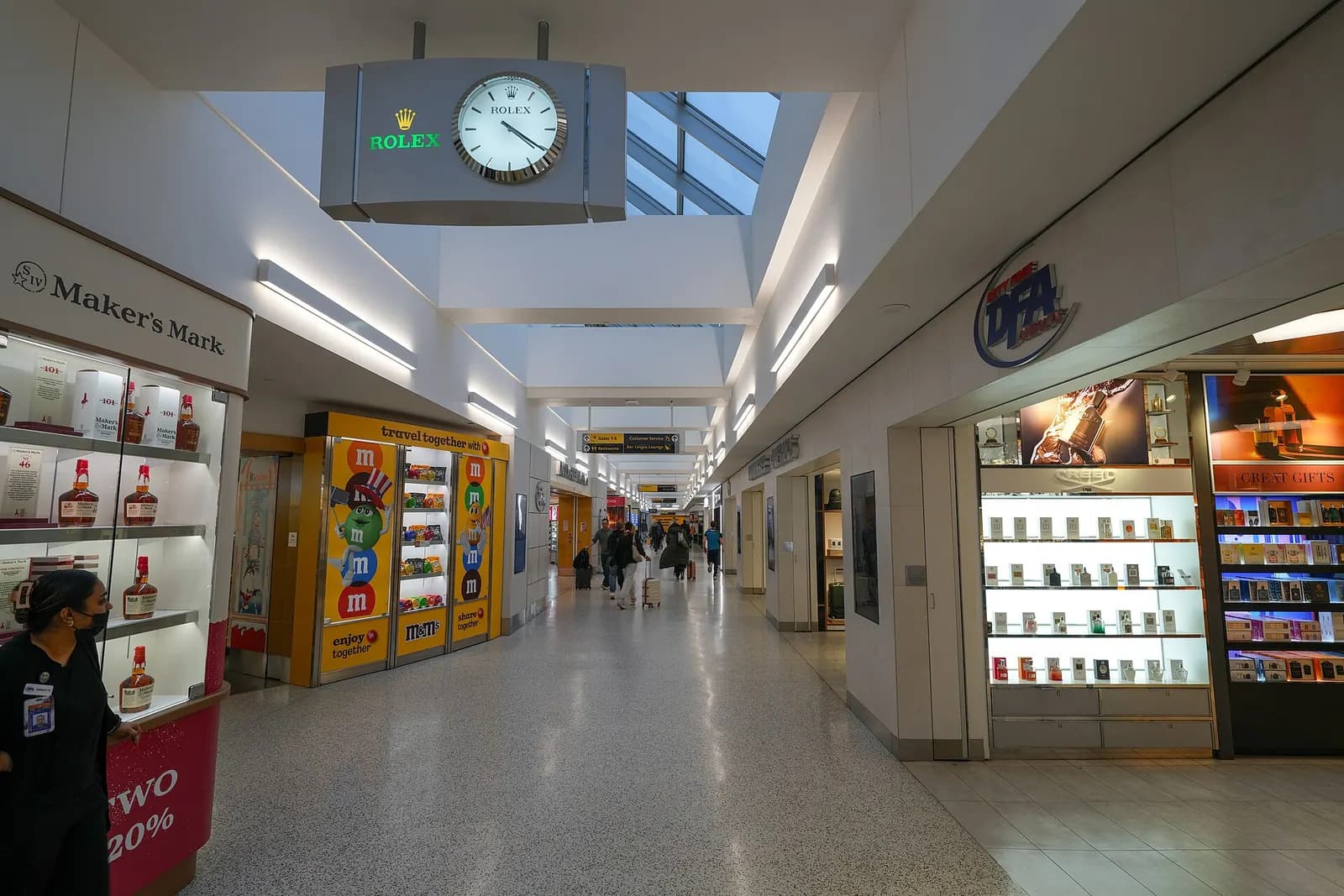 Inside Terminal 7's airside concourse, gate seating areas and retail shops line a wide hallway beneath a high ceiling.