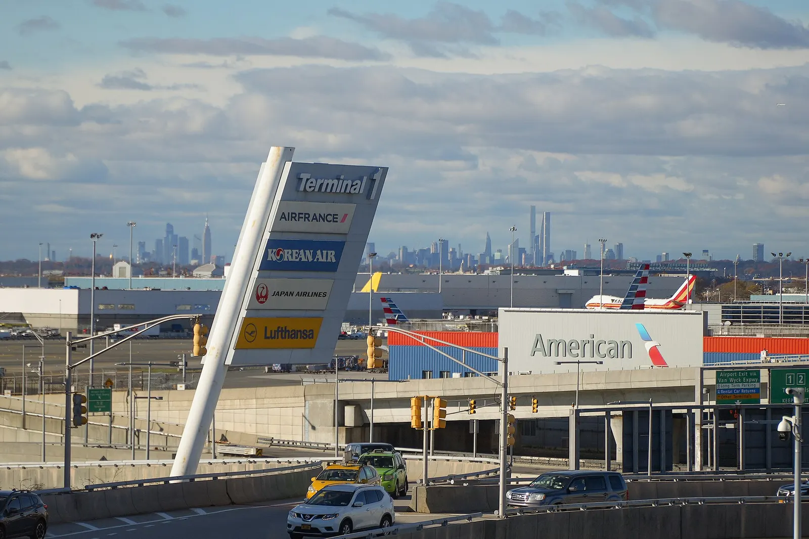 The Manhattan skyline is visible in the distance beyond the airfield, seen from Terminal One at JFK.