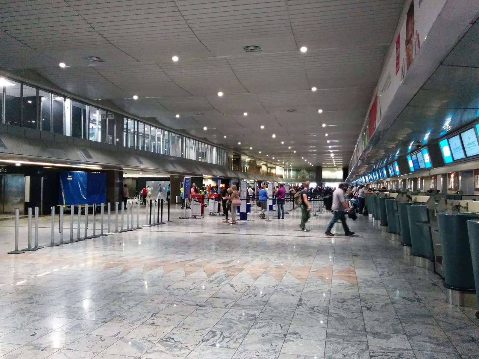 A wide view of the international check-in hall at O.R. Tambo International Airport with airline counters and travelers queuing with luggage.