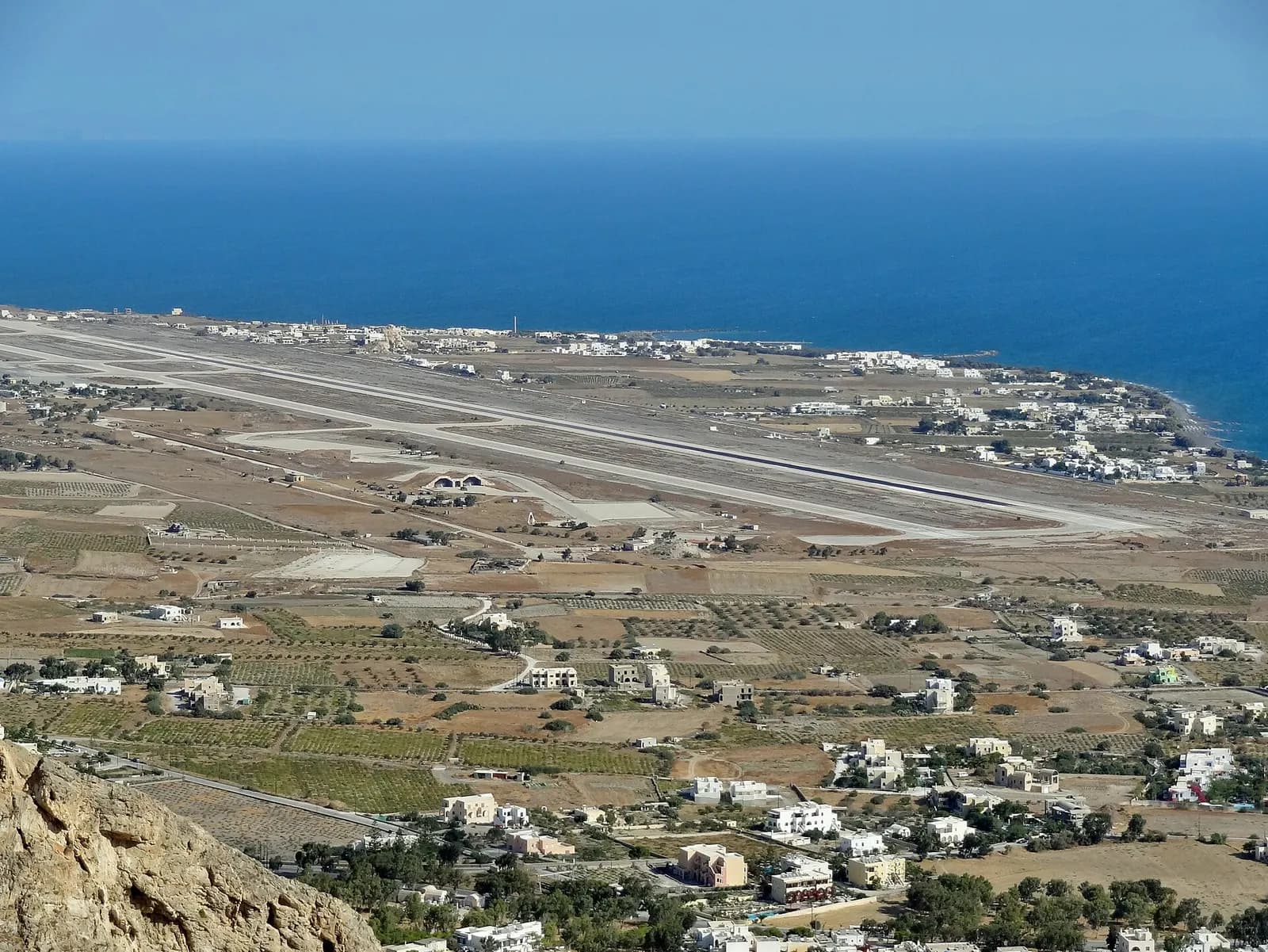 Elevated view of Santorini Airport runway parallel to the Aegean with Kamari-area settlements
