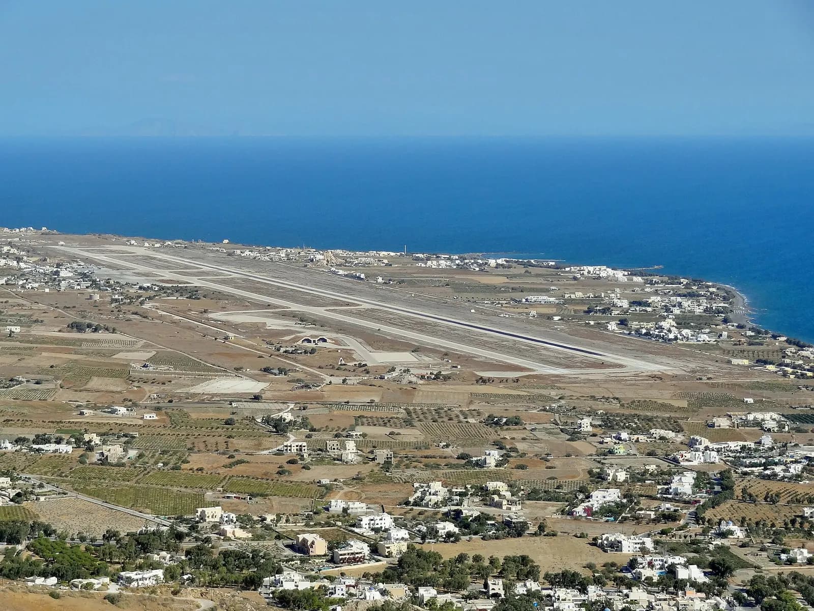 Santorini Airport apron and arched shelters on the coastal plain below Profitis Ilias slopes