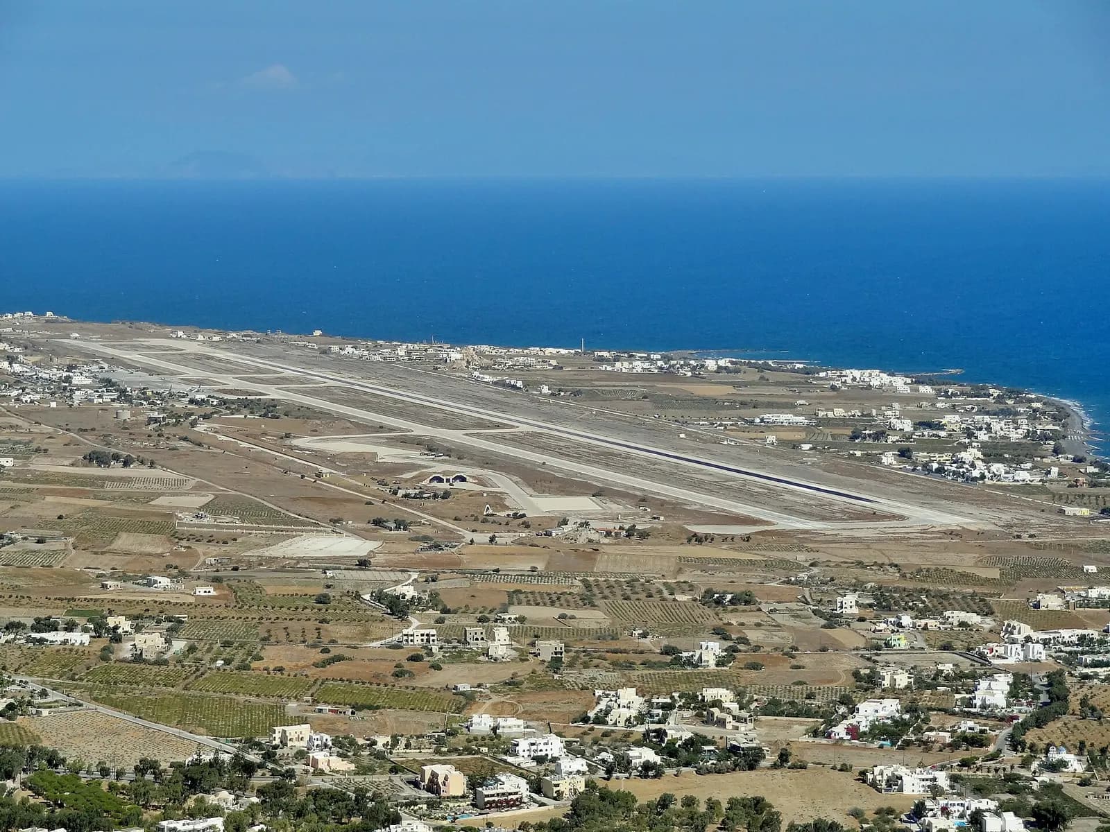 Wide elevated view of Santorini Airport single runway between vineyards and the Aegean Sea
