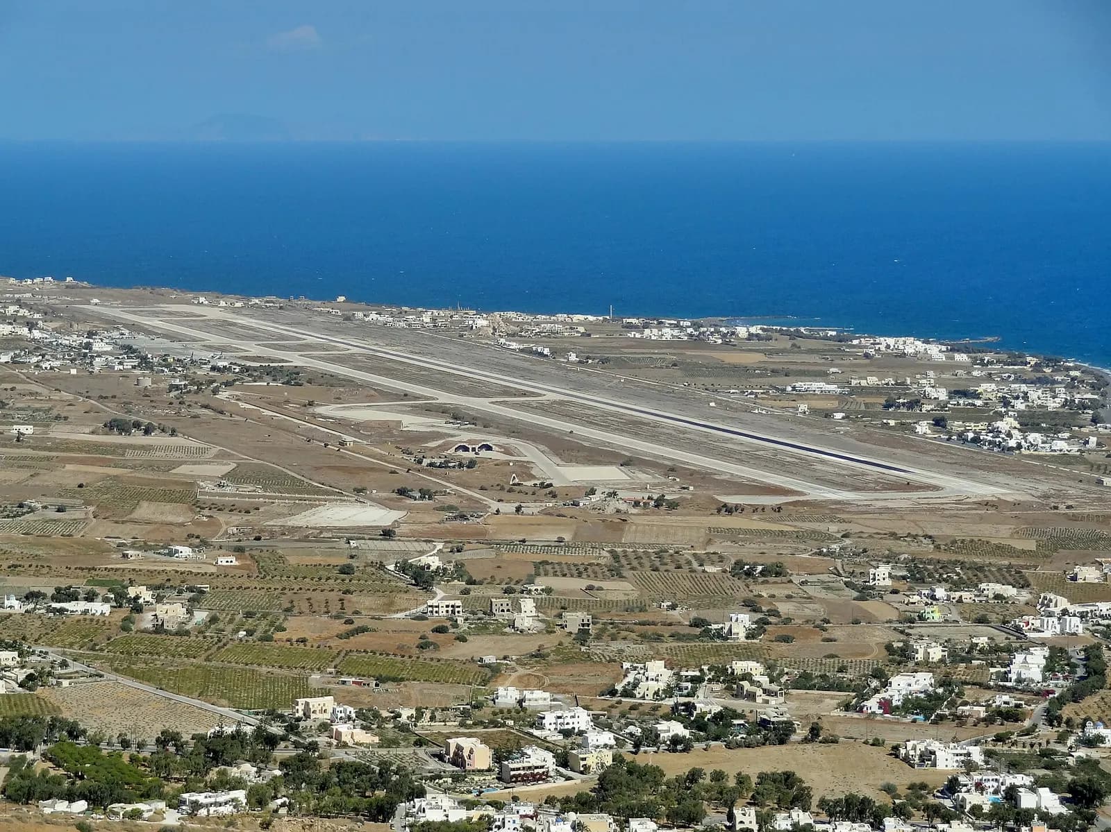 Santorini Airport terminal and apron cluster viewed from elevated inland terrain