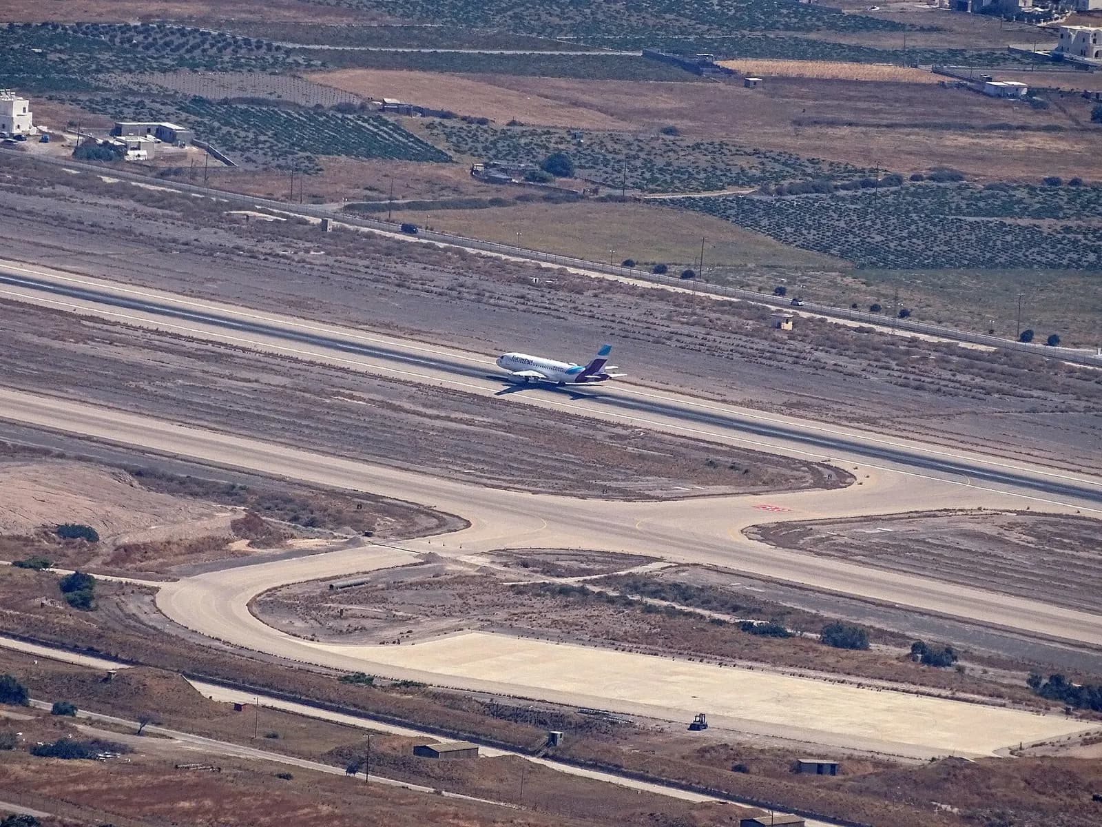 Eurowings narrow-body on Santorini Airport runway with Cycladic houses and volcanic hills behind