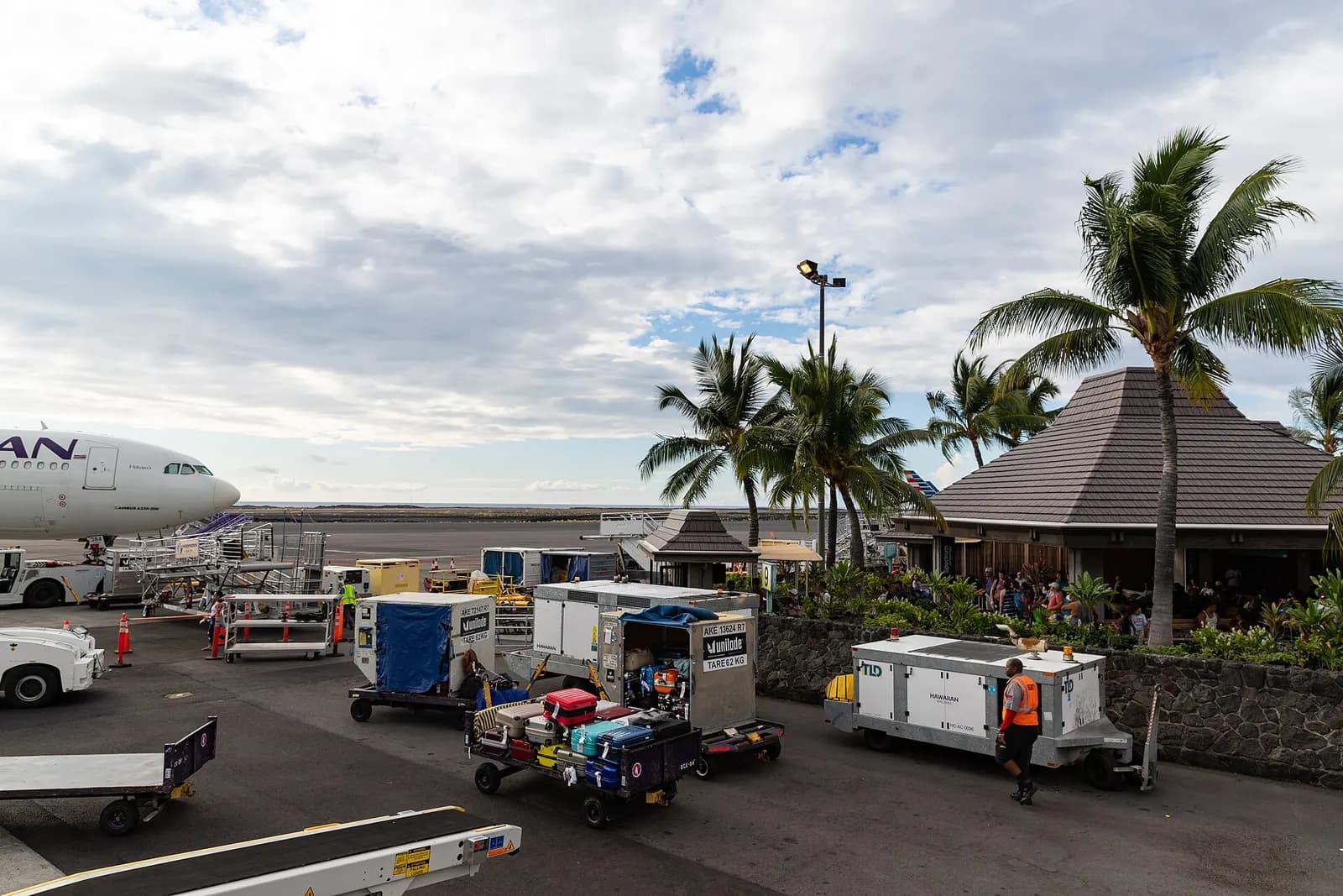 Hawaiian widebody on portable stairs at the open-air Kona pavilion, with ramp tugs